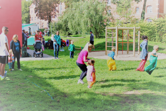 Kindern und Eltern hüpfen beim Sackhüpfen um die Wette.